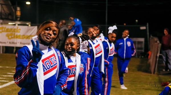 The cheerleaders, all dressed in blue and white uniforms, performing a dance routine on the football field.