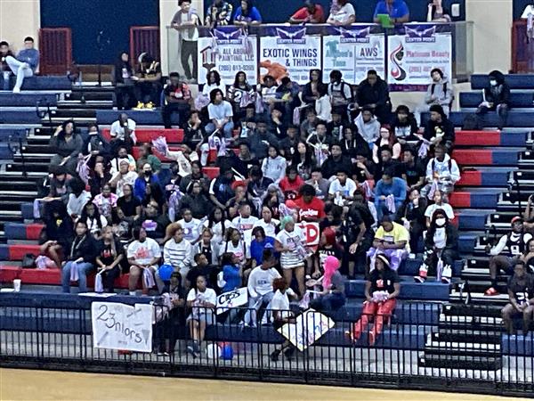 A large group of people gathered in an indoor arena, some holding signs, and one person standing on a stage.