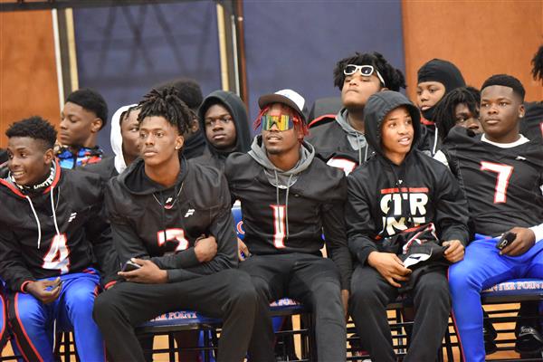 A group of male athletes seated in a line on a bench, dressed in sports uniforms and facing towards the camera.