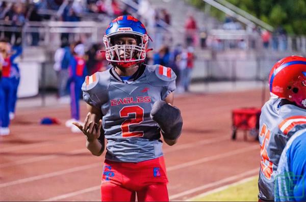 A football player in a grey uniform and red cleats, holding the ball on a field at night.