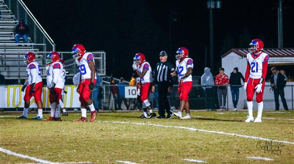 Seven uniformed football players on a field with grass and markings, waiting for the game to start.