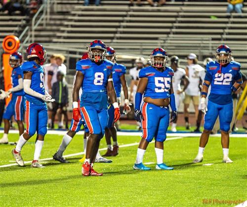 A group of football players in blue and red uniforms on the field, standing together with their hands on hips.