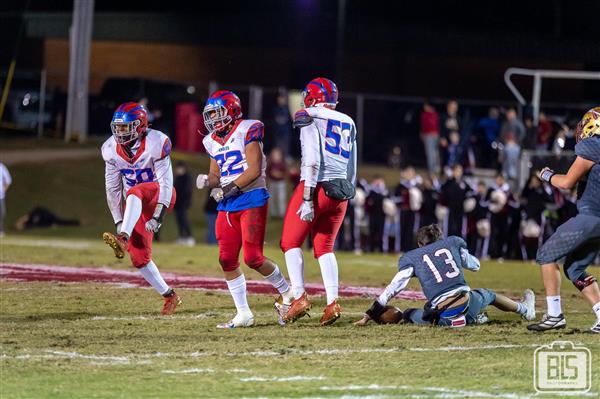 Vivid scene of a football game in action, featuring players in uniform running on the field under the stadium lights.