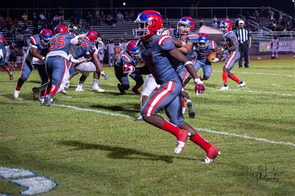 High school football game in action, with players running and the crowd watching.