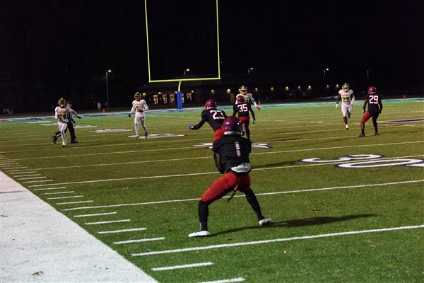 A football game in progress at night, with a player throwing a pass.