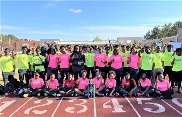 A group of people posing together on a track, all wearing matching brightly colored shirts.