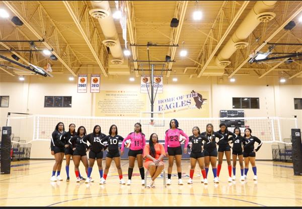 A team of women's volleyball players posing for a group photo inside an indoor gym.