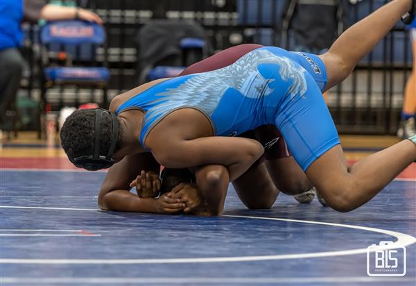 Two male wrestlers engaged in a competitive match on a blue wrestling mat.