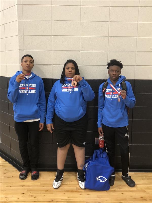 Three young men posing for a photo with sports uniforms, a medal, and a basketball.