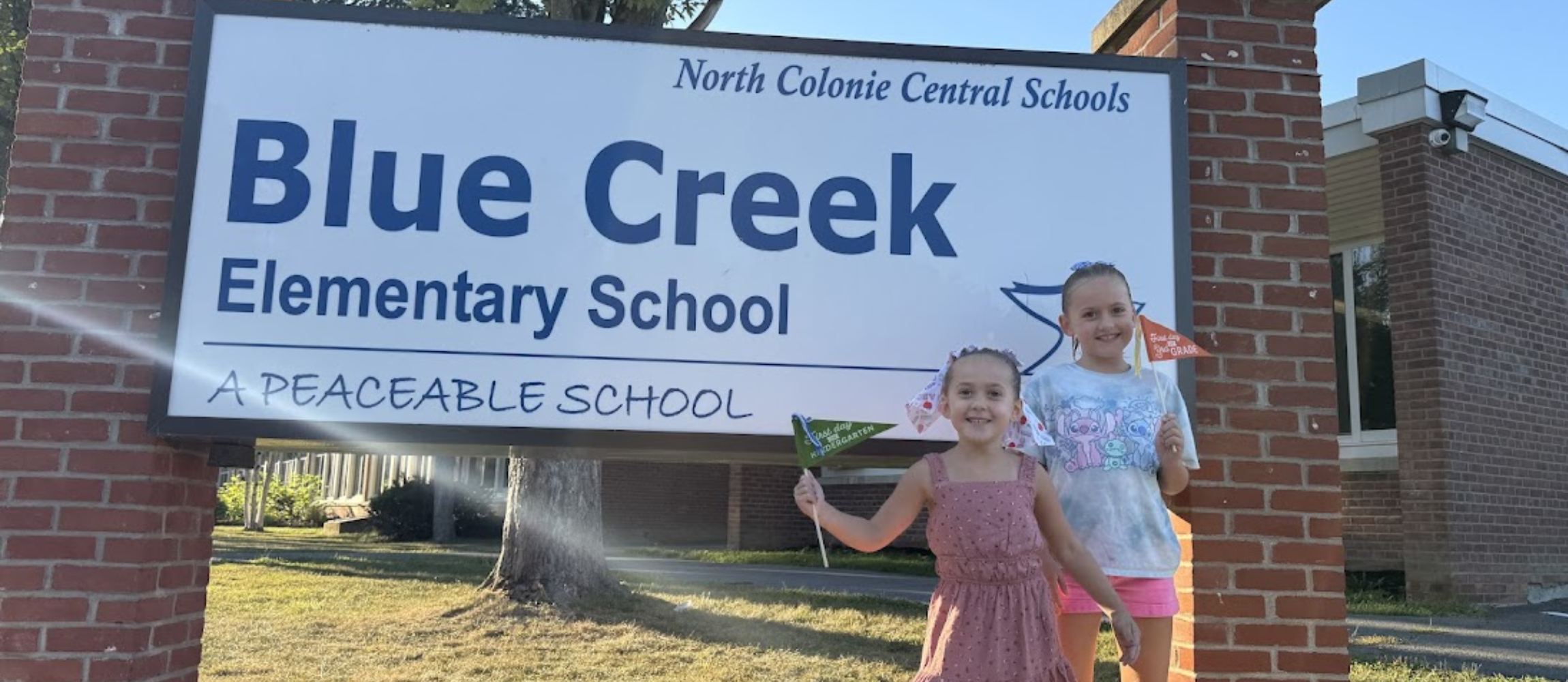 Two Blue Creek students smiling next to sign 