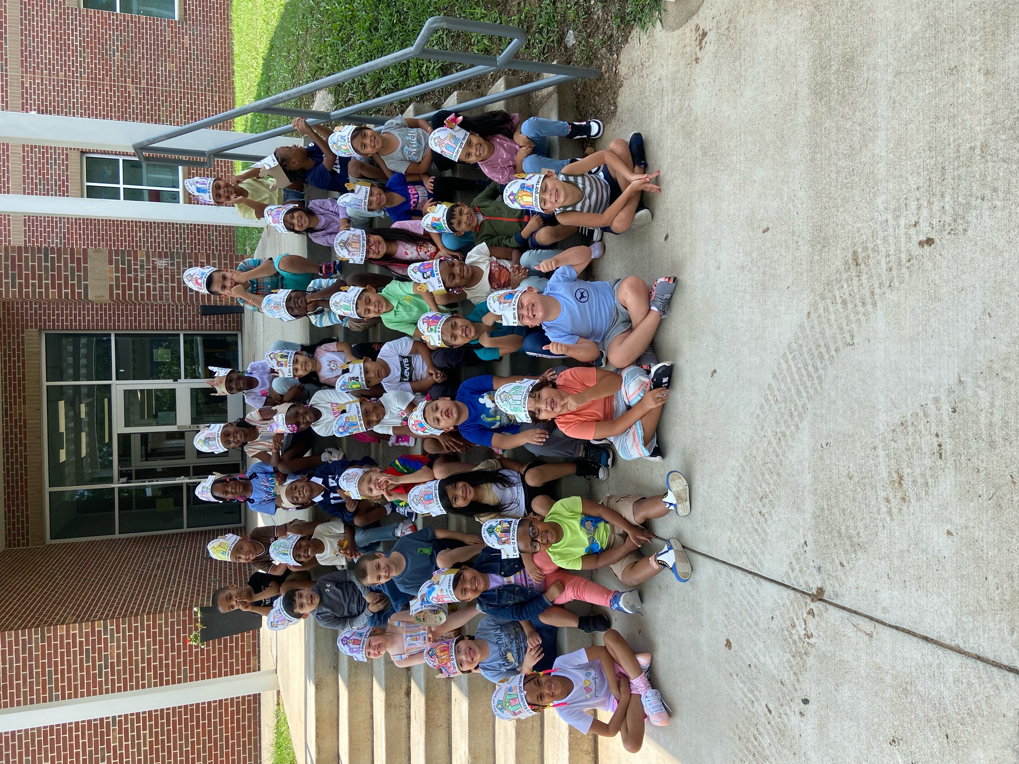 Kindergarten students sitting on steps wearing first day of school hats.