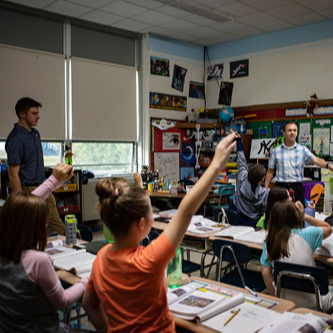 Students raise their hands in a classroom