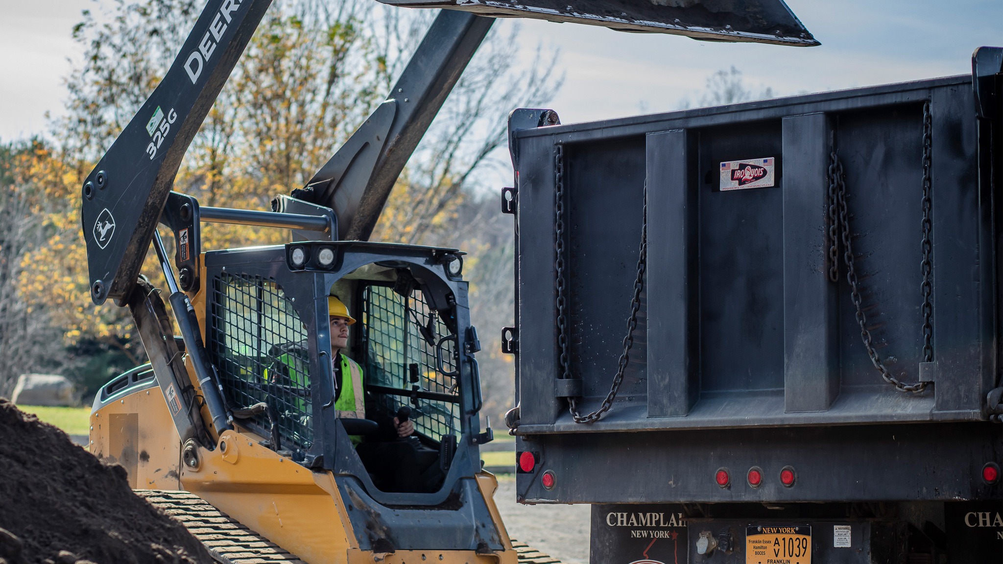 student using vehicle to pour dirt into dump truck