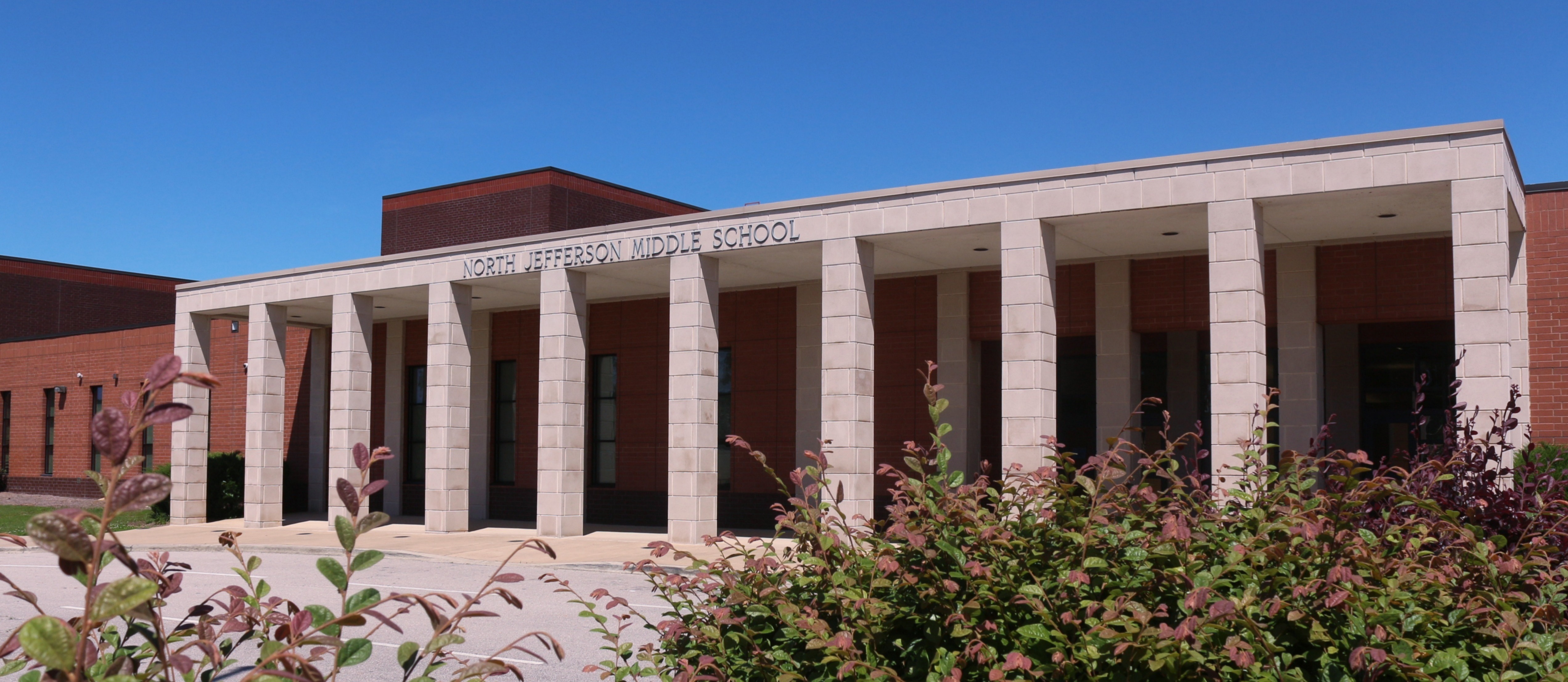 Front of North Jefferson Middle  School. It is a brick building with light colored columns in the front entrance. 