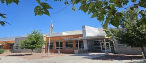 A modern building with several windows, a flag, and trees in front on a sunny day.