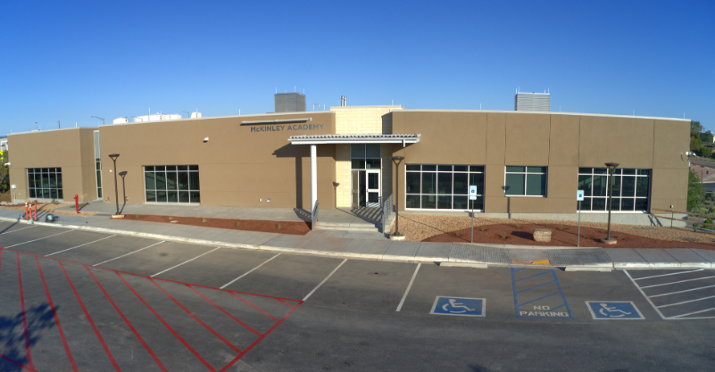 An exterior view of a single-story building with a flat roof, several windows, and a parking lot.