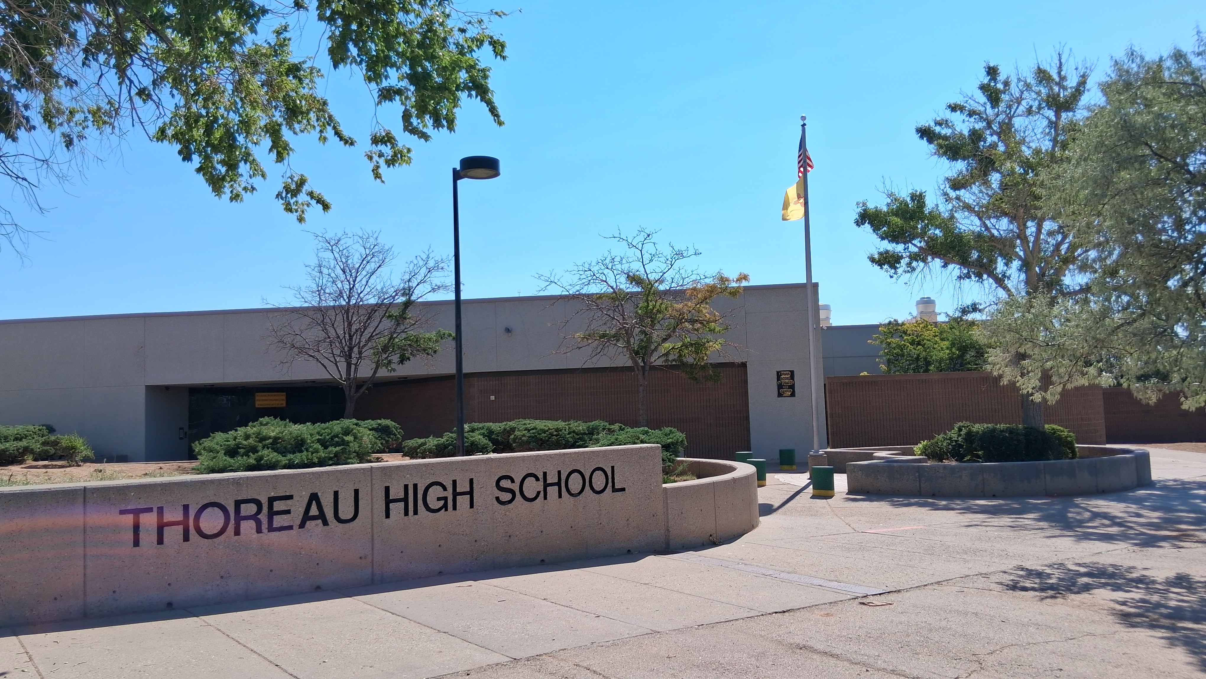 Thoreau High School letters on concrete wall, blue sky, green trees, flag on a flagpole