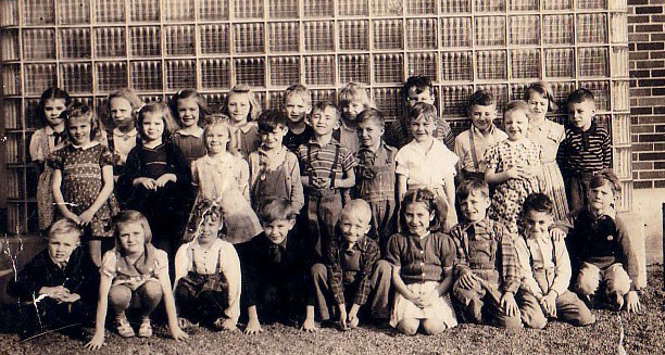 Students are posing in front of the orginal glass block windows on the south side of the building, the Kindergarten classroom.