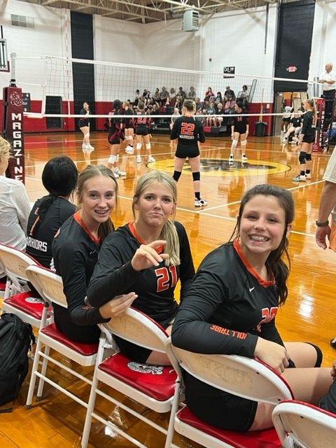 Three female volleyball players posing with their coach in a gym.