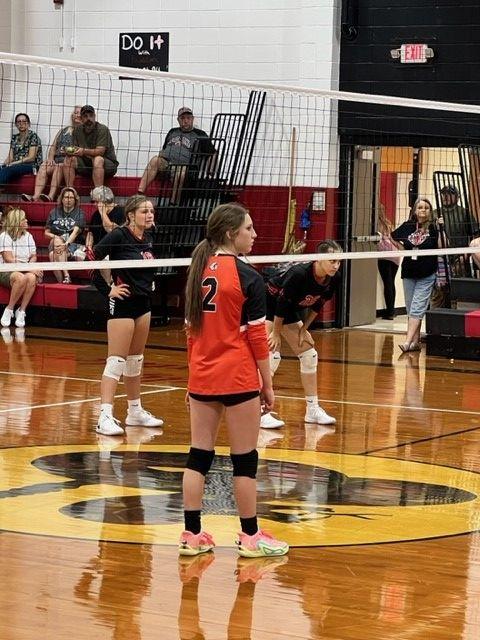 A female athlete standing on a basketball court during a volleyball game, waiting for the ball to be served.