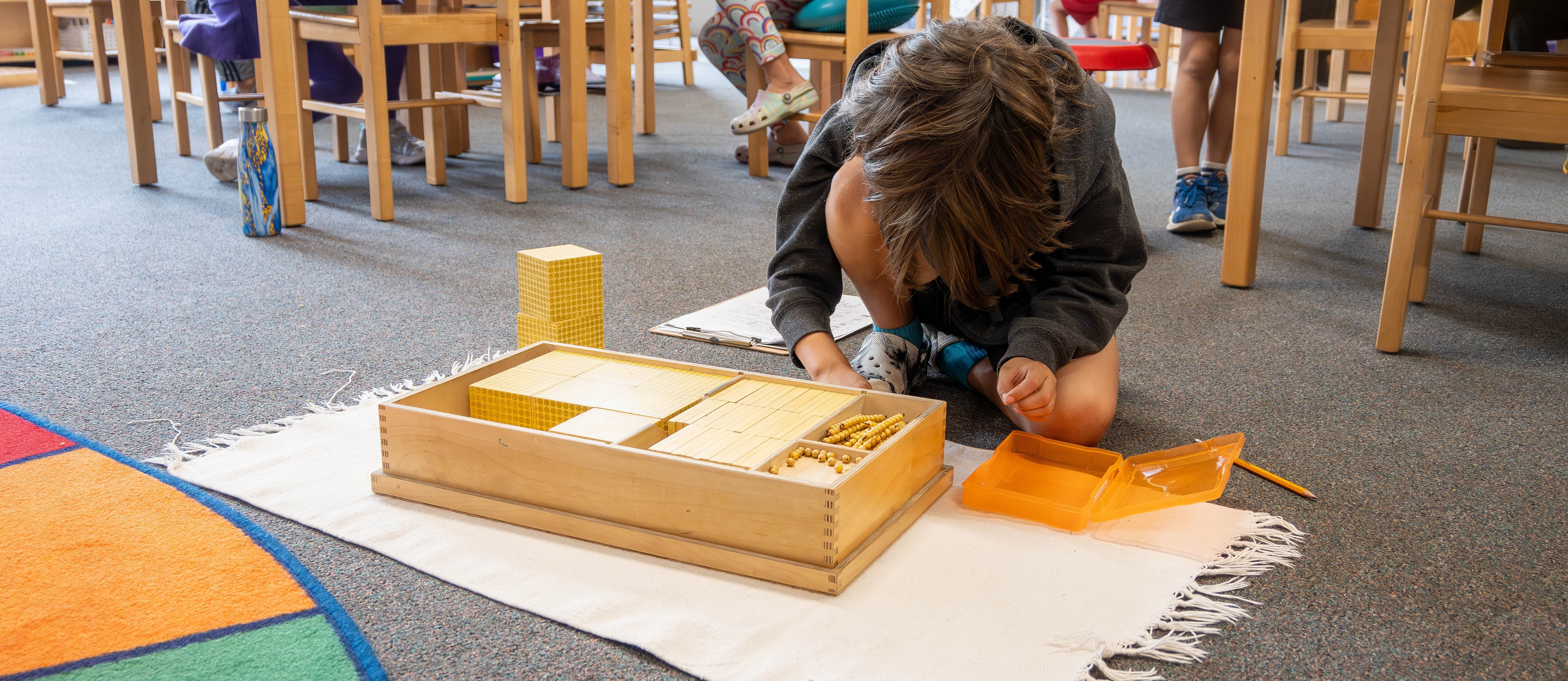 Picture of student working with Montessori base 10 material on rug