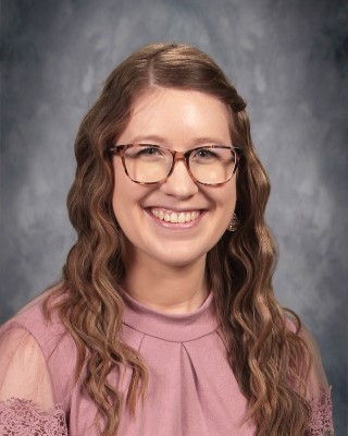 A smiling girl with glasses wearing a pink shirt, exuding a cheerful and friendly demeanor.