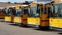 A row of yellow school buses parked neatly in a parking lot under clear blue skies.