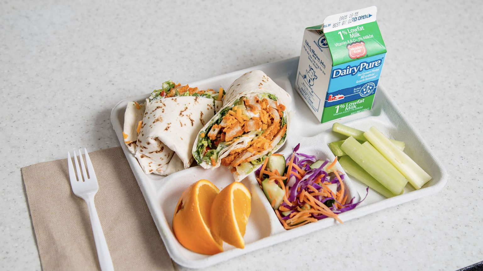 A tray featuring a sandwich, a fresh salad, and assorted fruit arranged neatly for a meal.