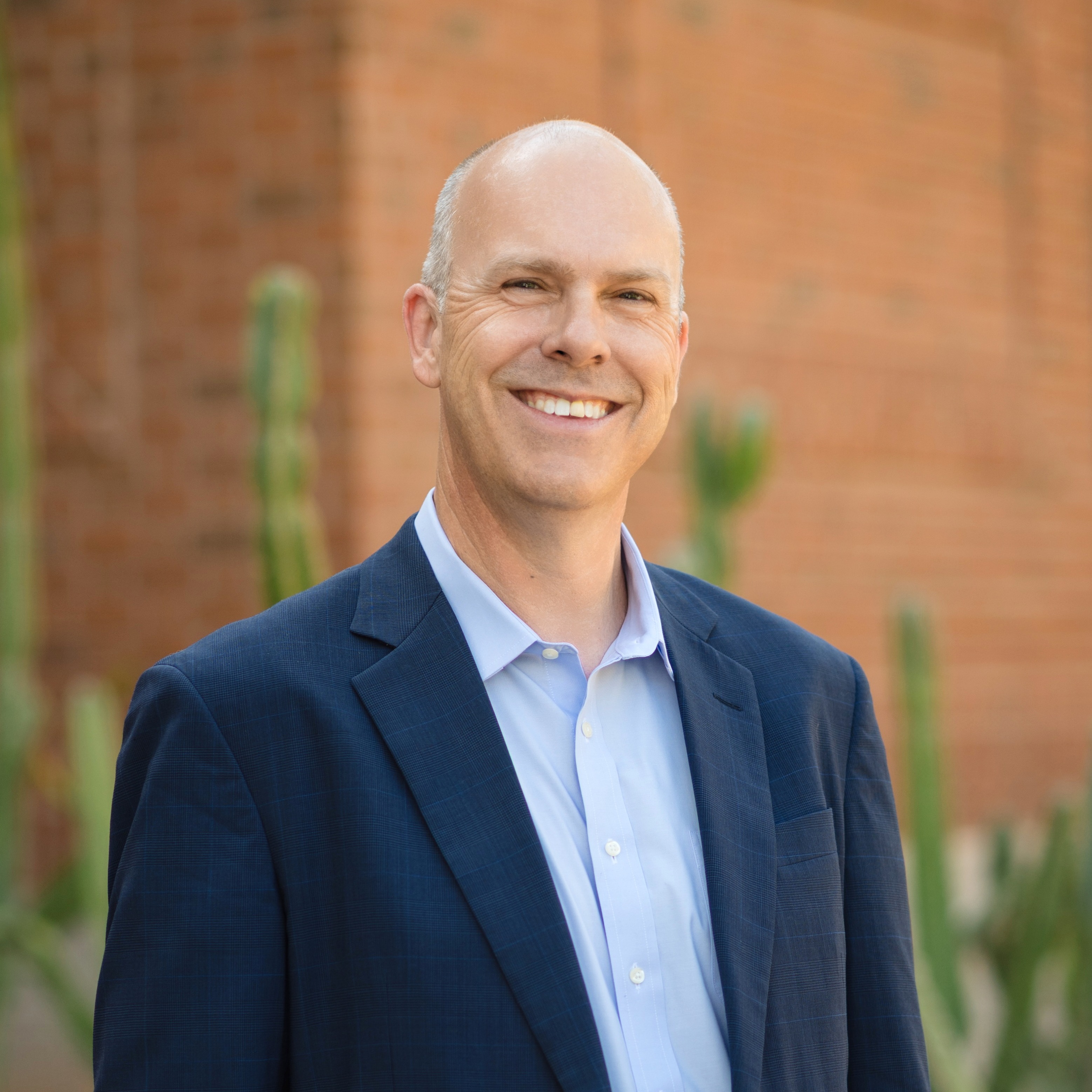 A man wearing a blue shirt smiles warmly at the camera, conveying a friendly and approachable demeanor.