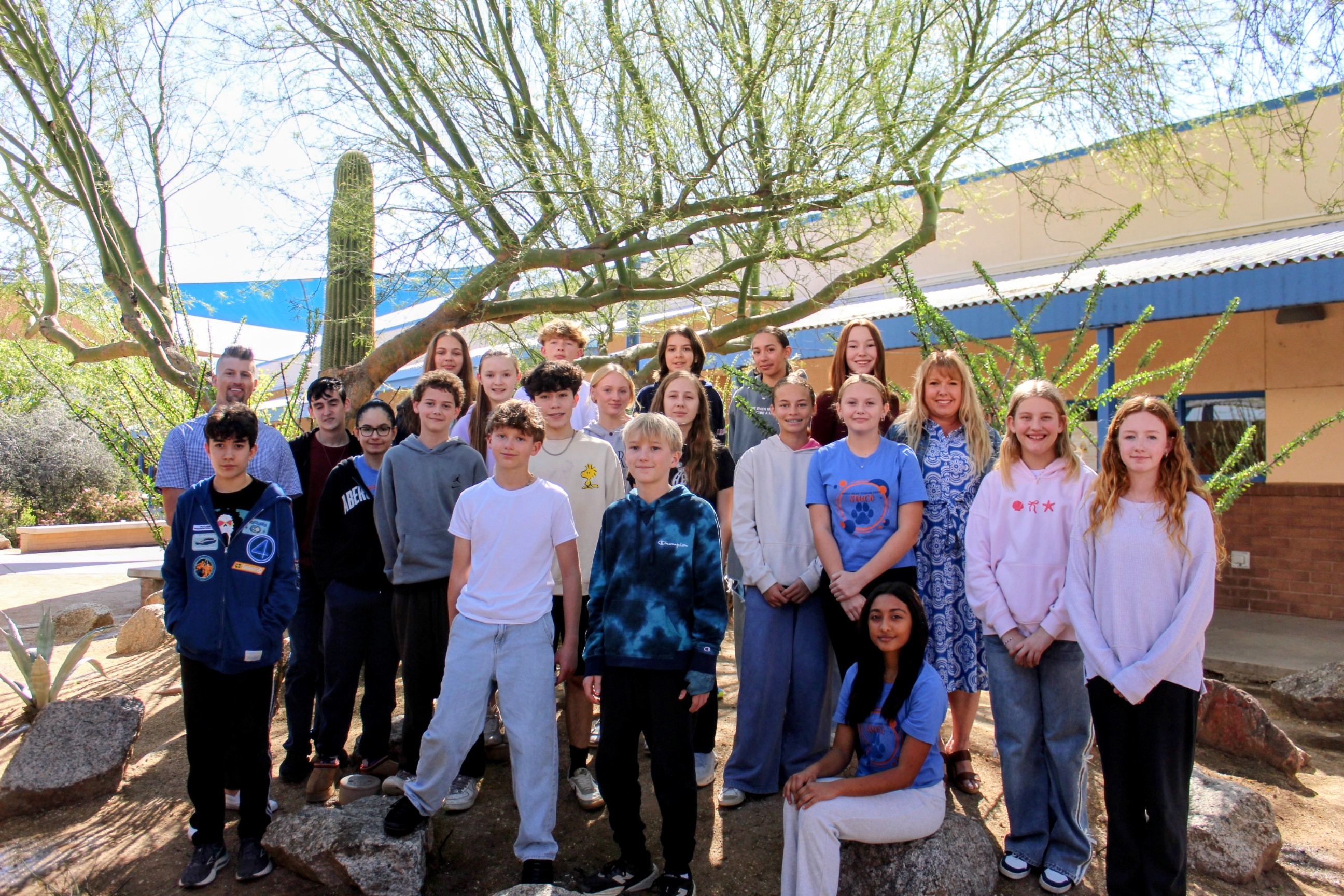 A group of people, possibly students, stand near rocks and a cactus in a courtyard.