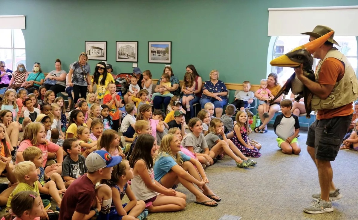 A mans hows a dinosaur puppet to a group of children.