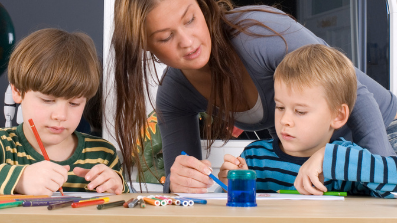 A teacher assisting two young boys with drawing activities.