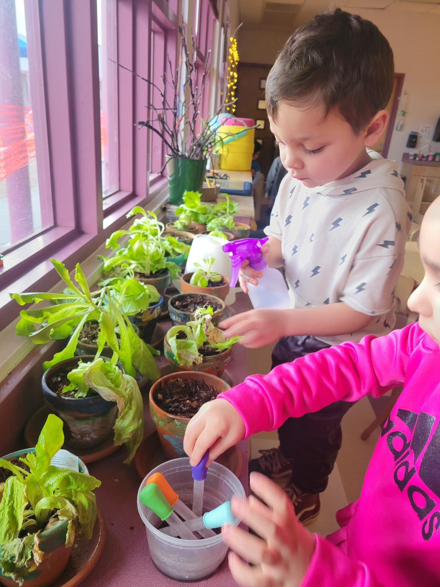 Two children planting seedlings in a classroom, surrounded by pots and gardening tools, engaged in hands-on learning.