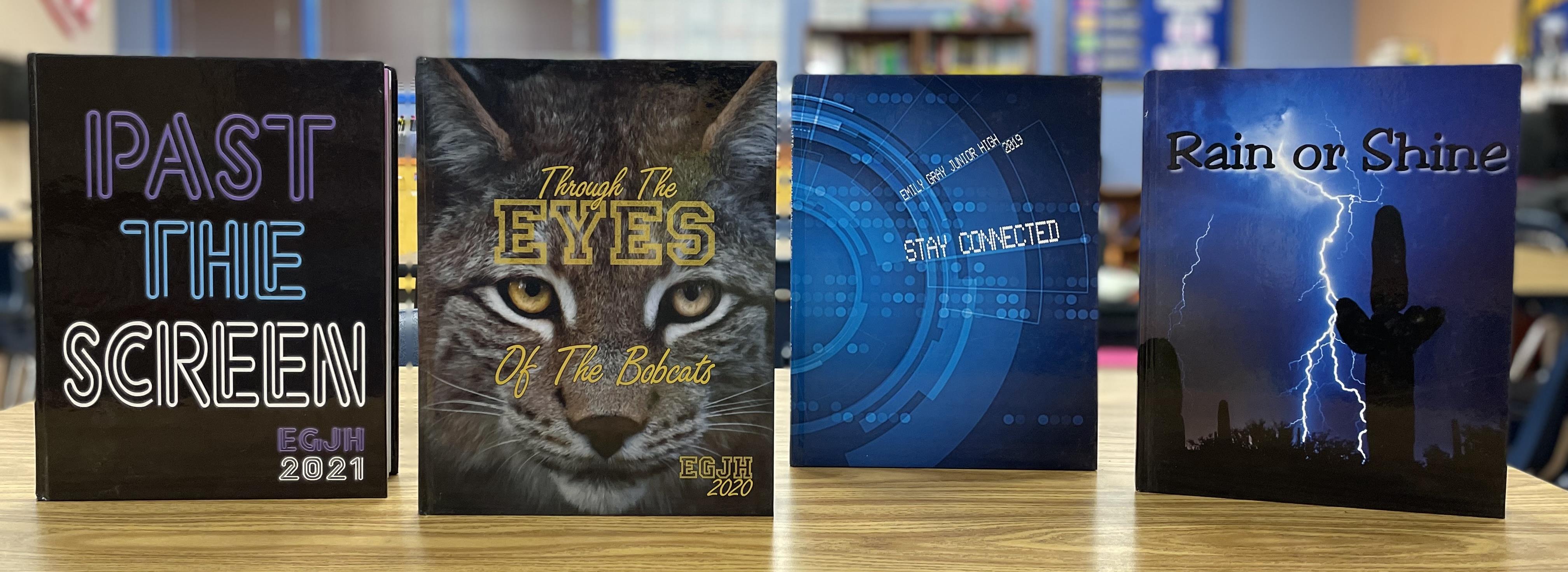 Four yearbooks displayed on a table: "Past the Screen" (2021), "Through the Eyes of the Bobcats" (2020), "Stay Connected" (2019), "Rain or Shine."