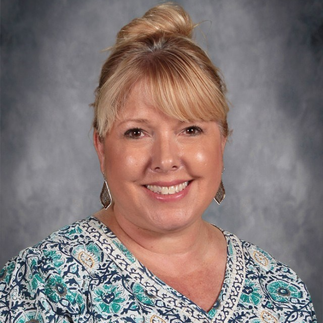 A woman wearing a floral shirt smiles brightly at the camera, exuding warmth and positivity.
