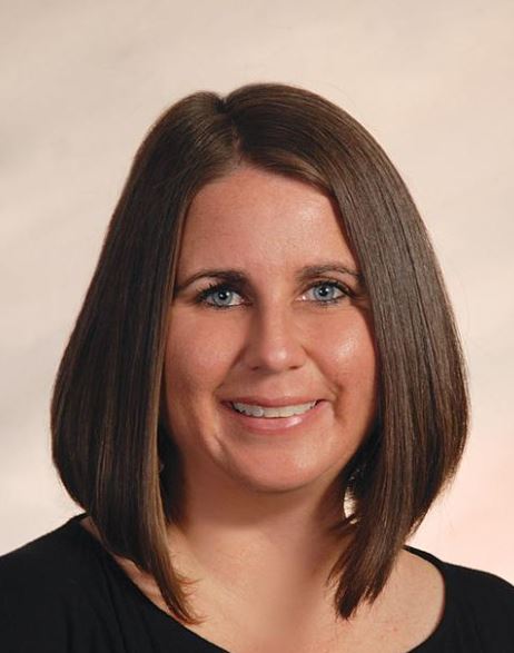 A woman with sleek, straight, medium-length hair, wearing a black top, posed against a soft, neutral background.