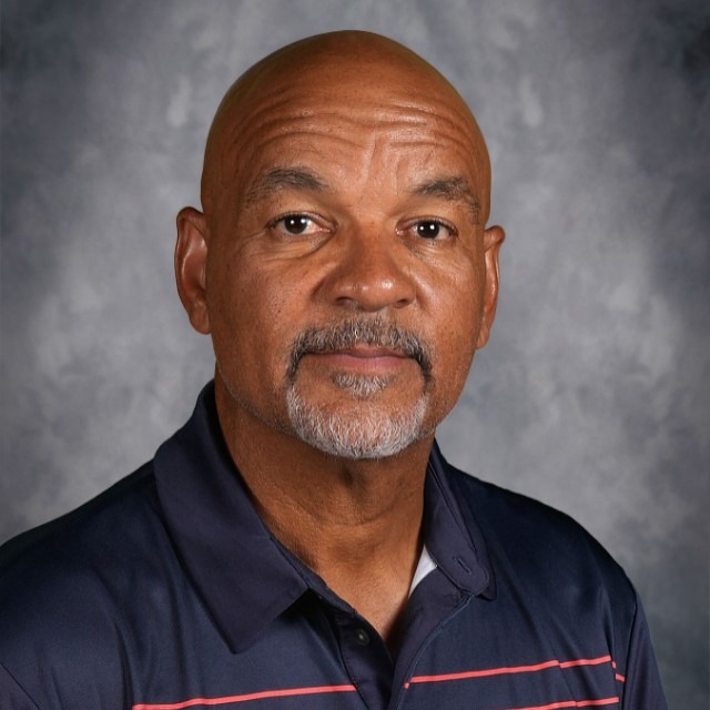 A man wearing a patterned dark shirt poses against a neutral grey background.