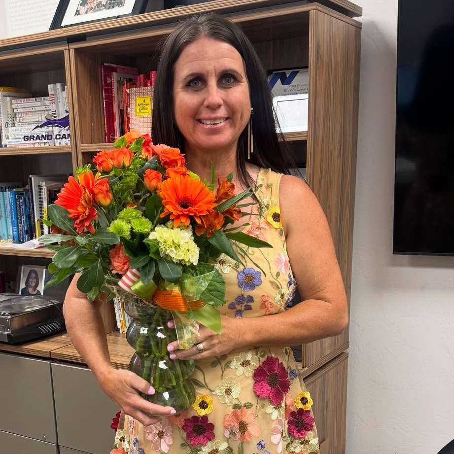 A woman with sleek, straight, medium-length hair, wearing a black top, posed against a soft, neutral background.