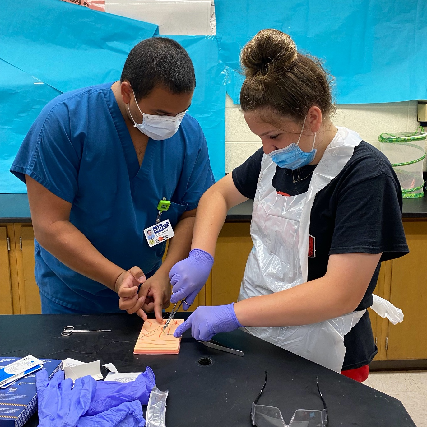 resident assists student with suturing