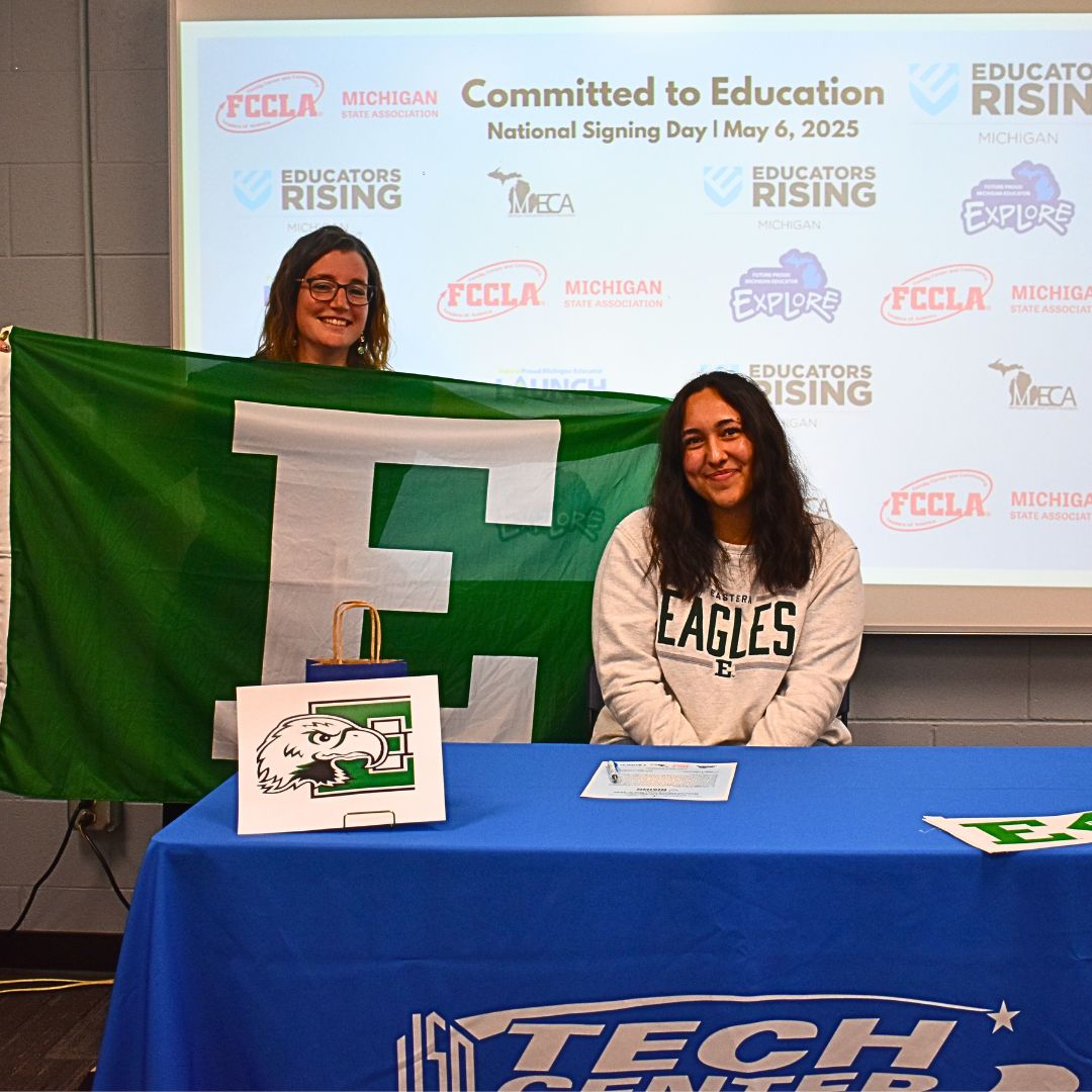 Student signing with teacher holding Eastern Michigan sign behind her