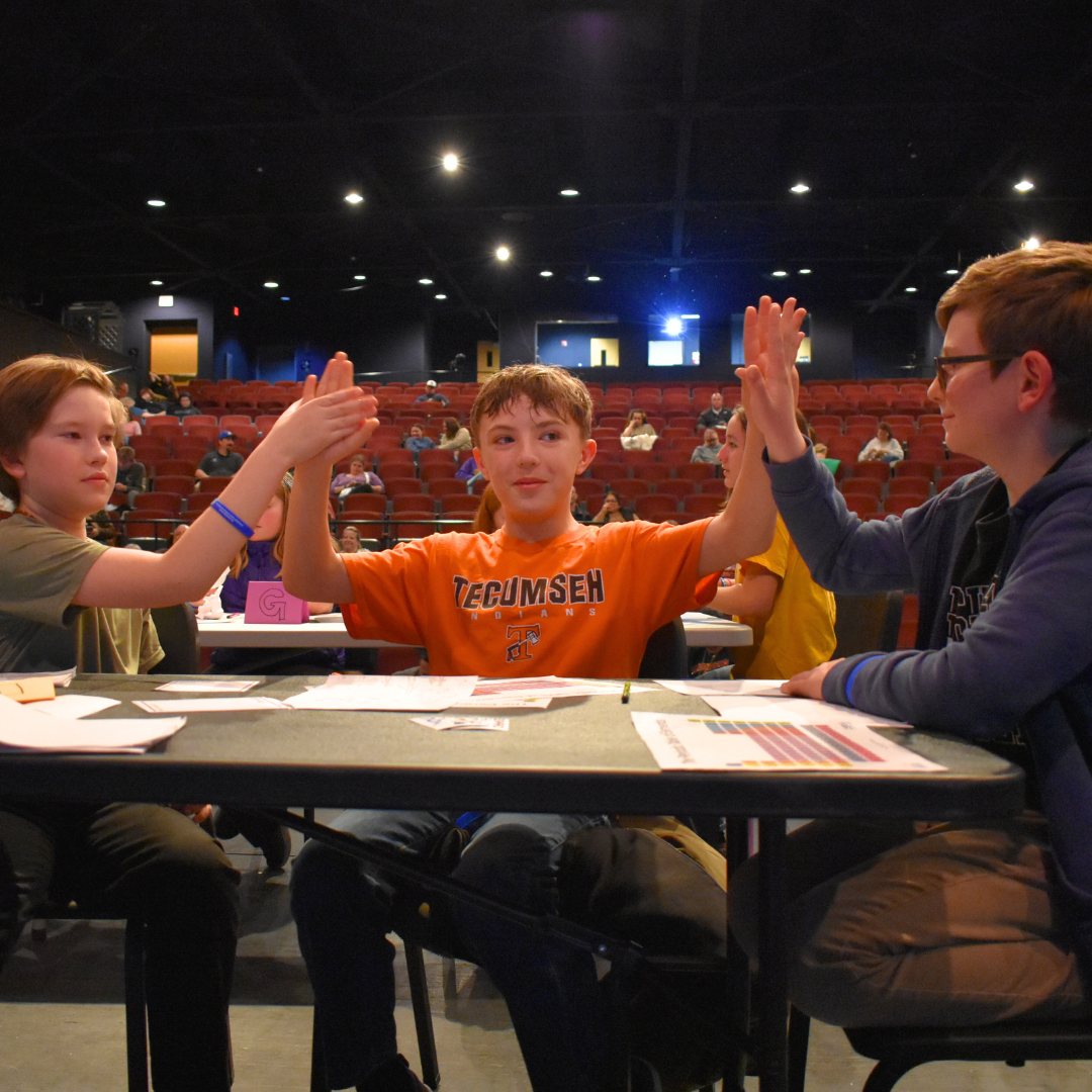 A photo of three students giving each other a high-five after answer a correction correctly