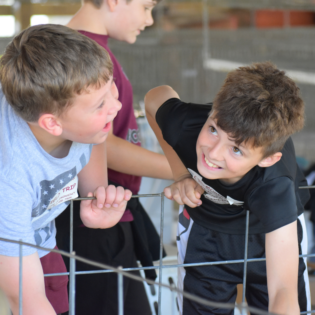 Two students smiling as they reach in to pet a goat at Project RED