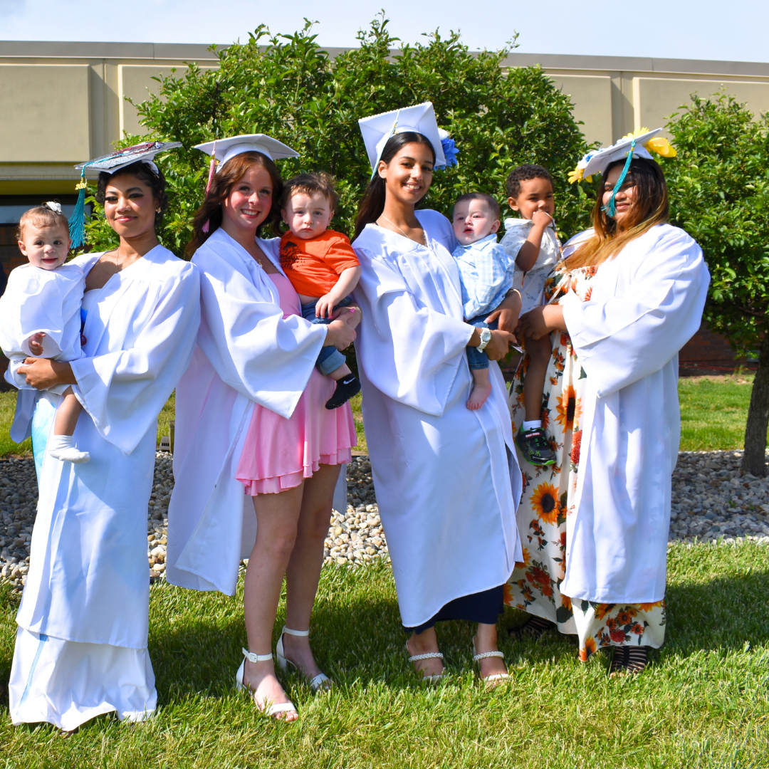 The four PREP graduates holding their children while in their caps and gowns