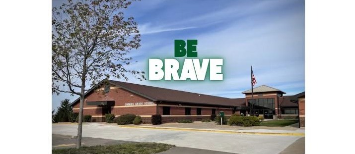 The brick exterior of Dimmick Grade School under a blue sky with the words BE BRAVE overlaid in large, bold, white and green text above the building.