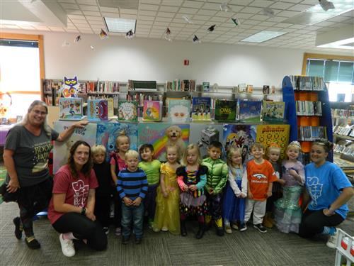 Children, adults, and a dog at an indoor event, standing in front of a colorful backdrop.