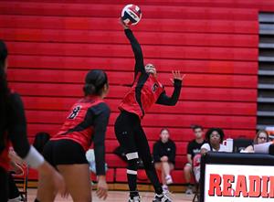A woman in a red jersey is throwing a volleyball on an indoor court.
