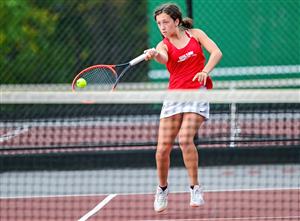 Woman holding a tennis racket and preparing to hit a tennis ball on the court.