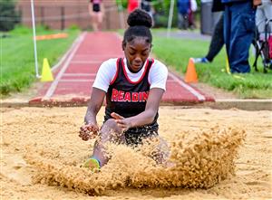 Woman athlete leaping with sand kicked up behind her.