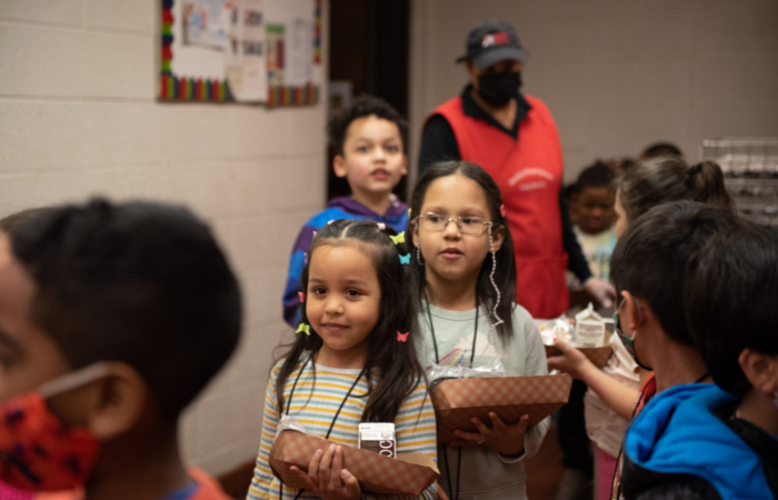 group of children and adults interacting in a room, with some people standing around while others are seated and engaged in activities.