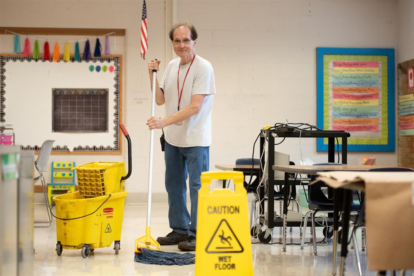 Person cleaning with a mop in front of school supplies and an American flag.